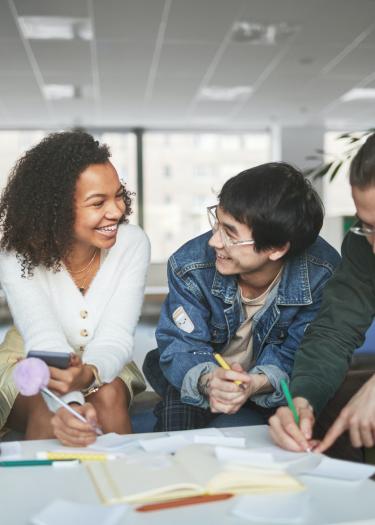 4 Studierende unterschiedlicher Ethnizitäten sitzen an einem Tisch
