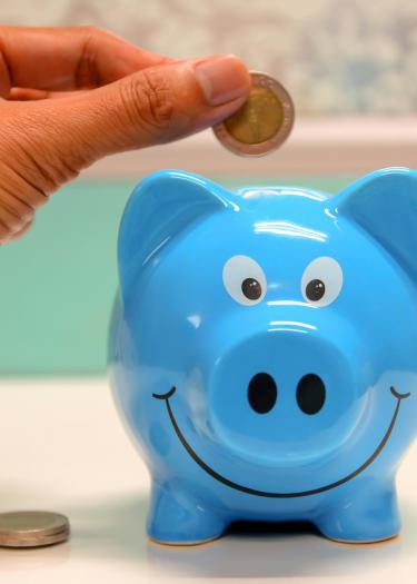 Eine 2-Euro-Münze wird in ein blaues Sparschwein gegeben